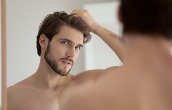 A young man looking at a mirror and checking his hair.
