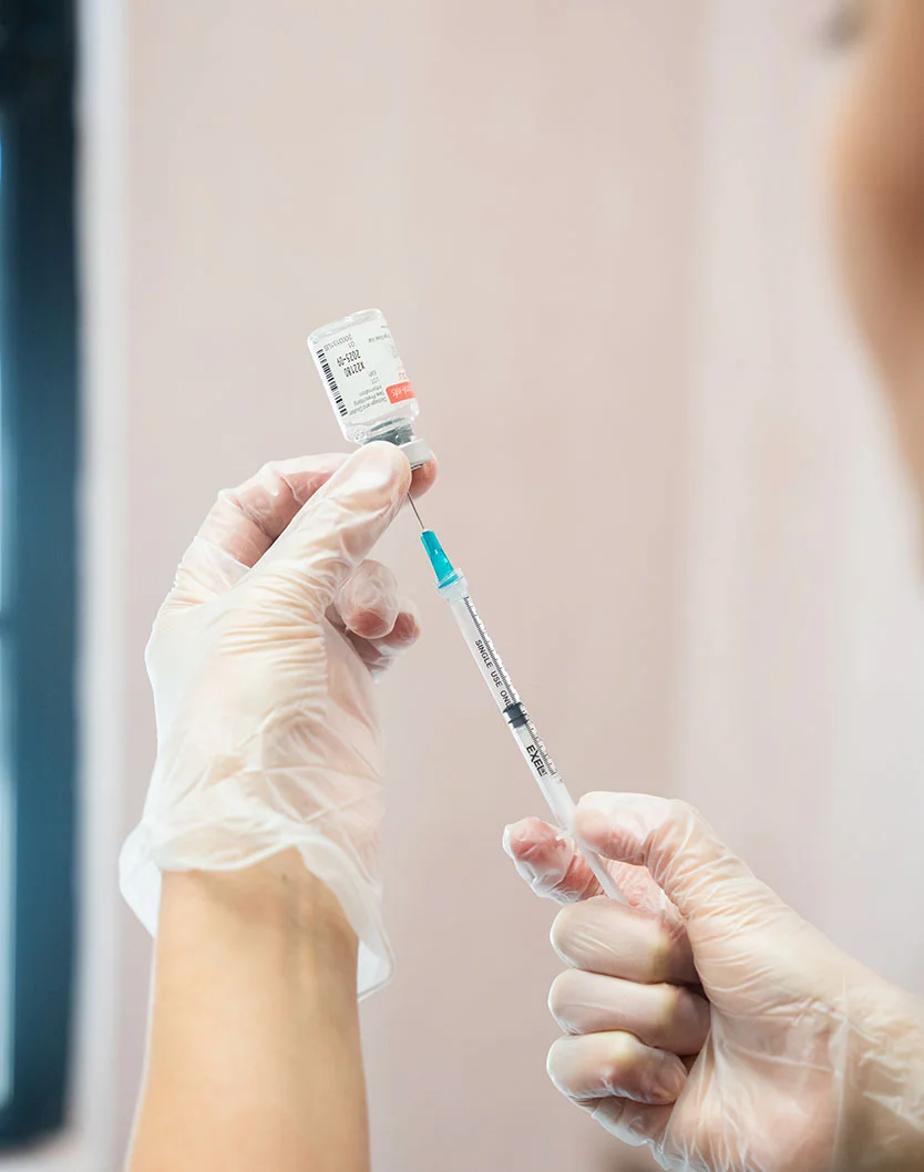 A gloved hand holds a syringe, preparing to draw liquid from a vaccine vial in a clinical setting. - Botox and Wrinkle Relaxers in New York, NY