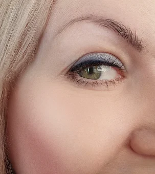 Close-up of woman's eye with blue eyeshadow and blonde hair showing makeup application technique