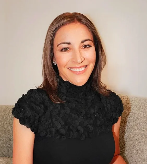 Professional woman in black dress with textured collar smiling at camera in indoor setting