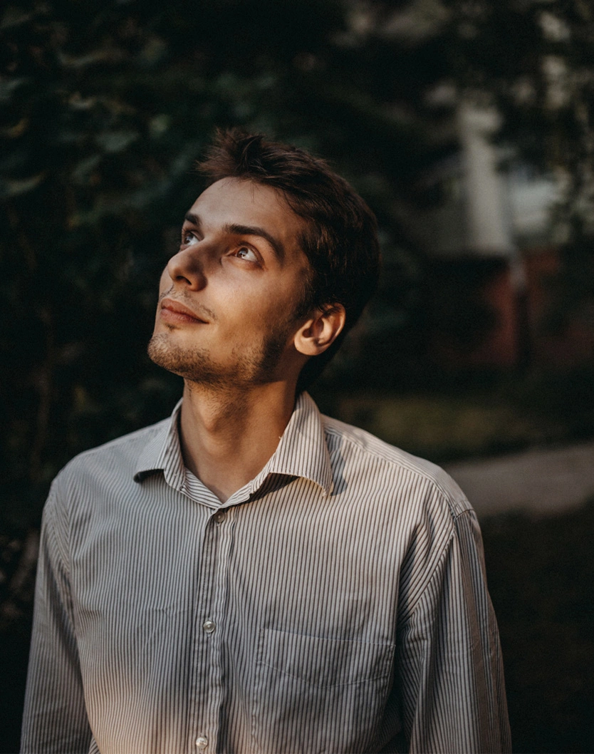 Young man in white shirt looking up thoughtfully outdoors with natural lighting and blurred background