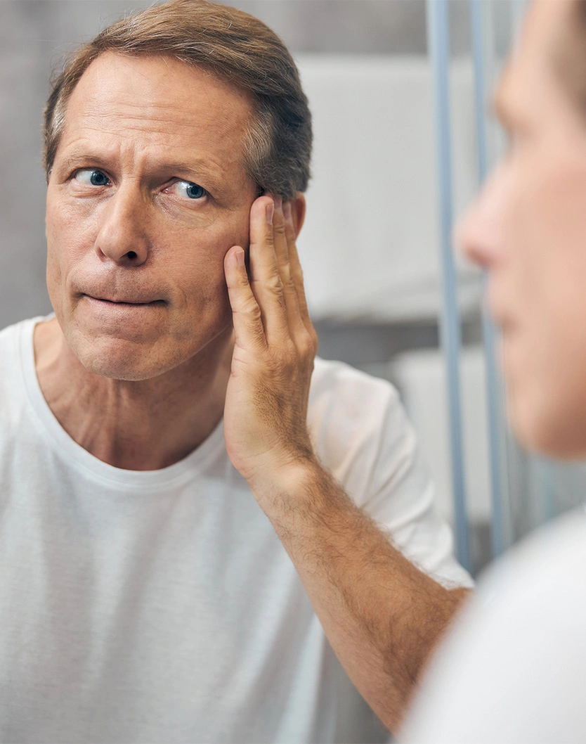Man examining his face in mirror checking skin for signs of aging or skin concerns