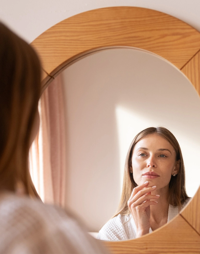 Woman examining her neck and jawline in round wooden mirror during skincare routine