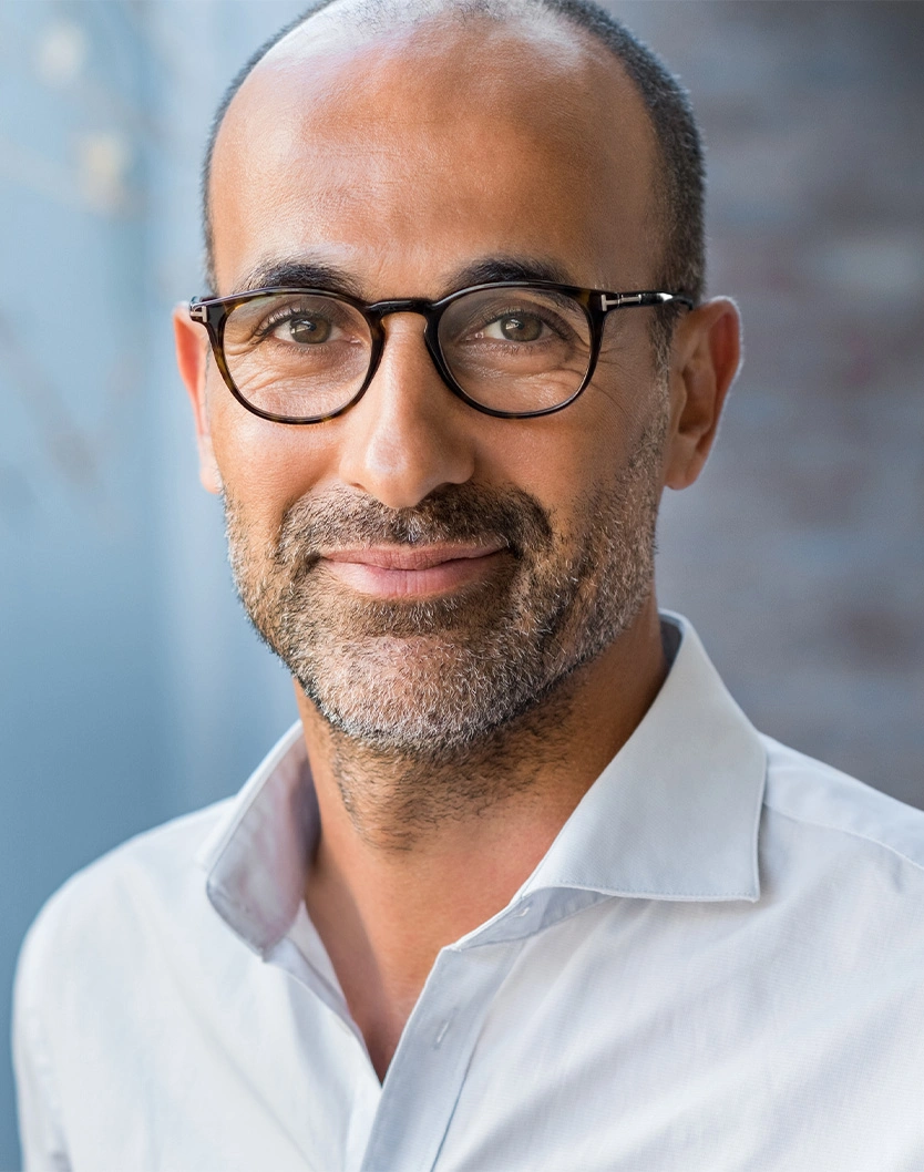 Professional headshot of smiling bald man with glasses and gray beard wearing white collared shirt