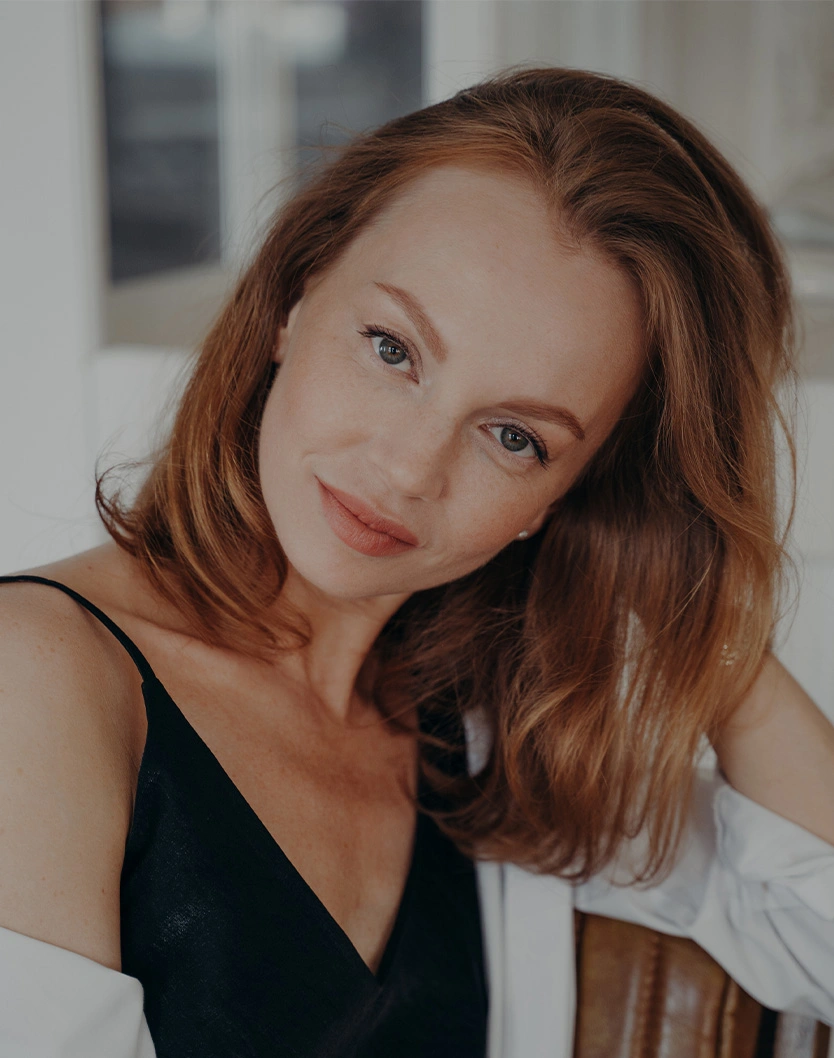 Young woman with shoulder-length auburn hair wearing black dress, natural makeup and subtle smile in portrait photo