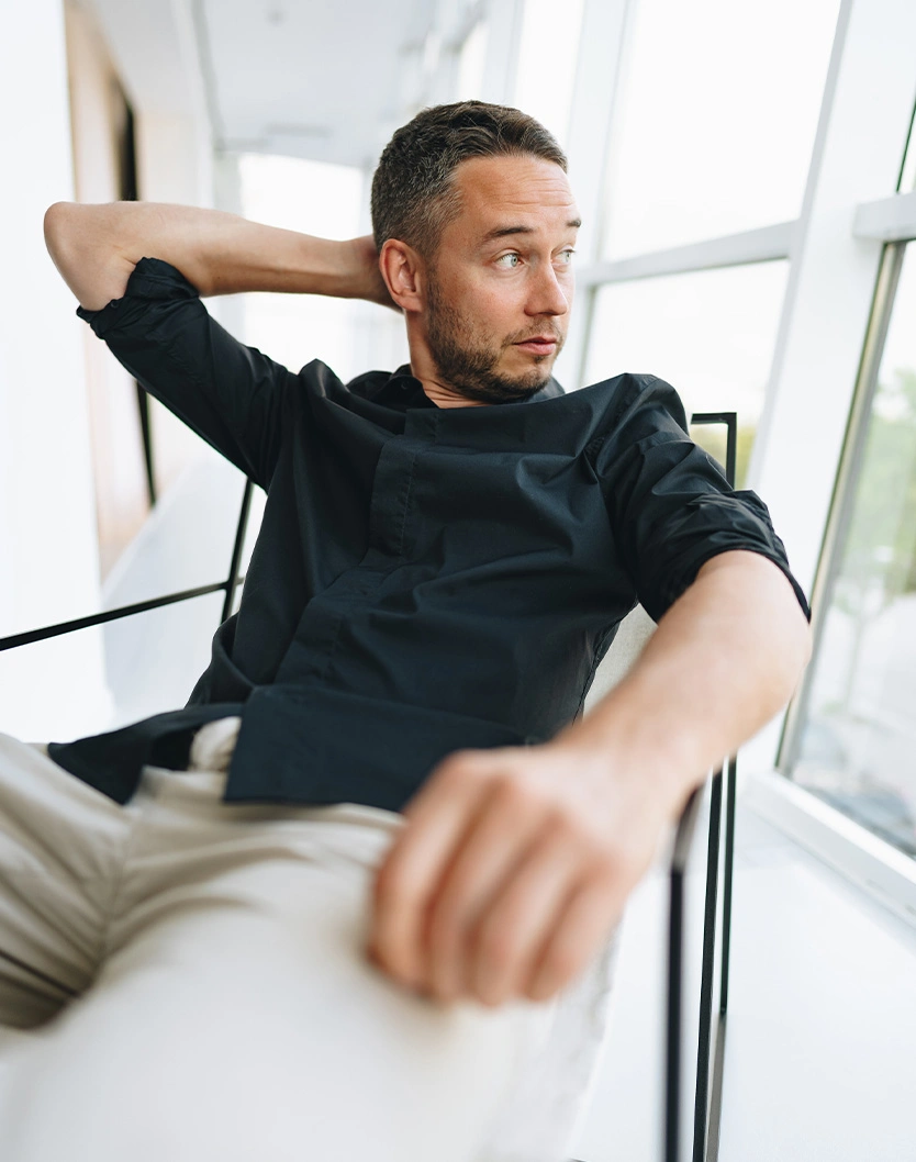 Man in black t-shirt relaxing in modern white office chair near window with natural lighting