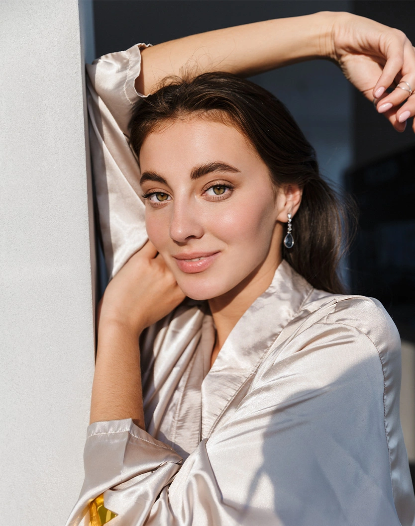 Professional woman in white blazer posing with hand on chin in modern studio setting