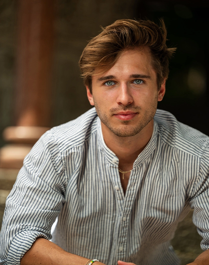Young professional man in striped button-down shirt with styled hair looking at camera in warm indoor setting
