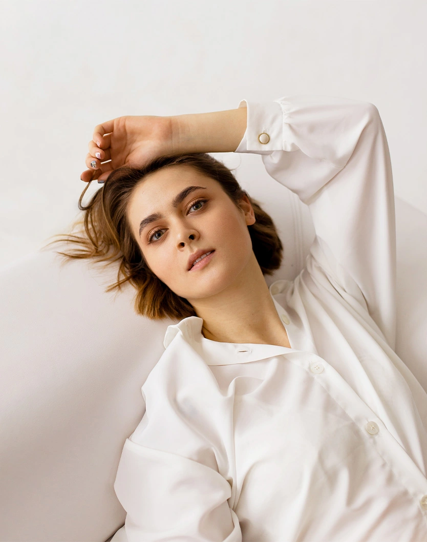 Woman in white shirt with hand in hair posing against neutral background in natural light portrait