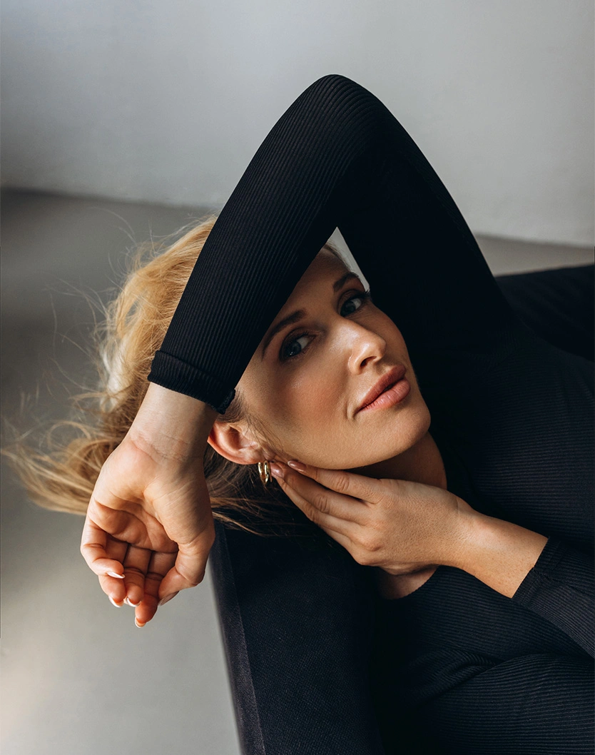 Woman in black long-sleeve top with arms raised above head looking up in artistic portrait pose